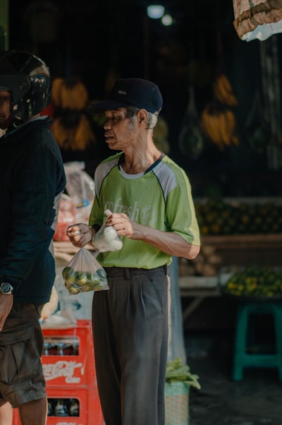 人在绿色水手领衬衫和黑色夹克拿着白色的塑料袋
